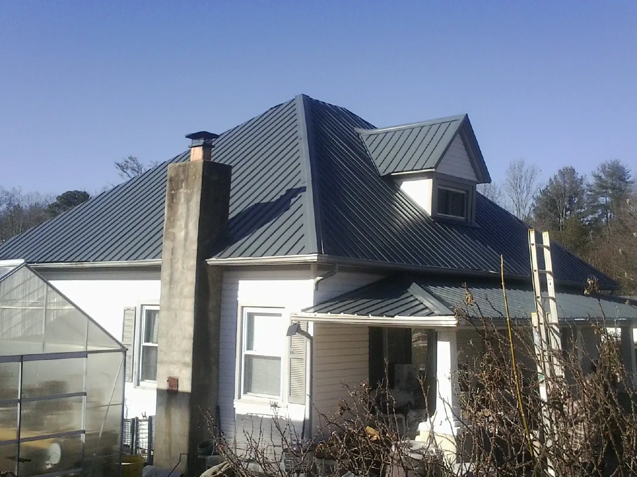 Dark blue standing seam metal roof on a white farmhouse with dormer — Slate & Tile Roof Repair by Roofing Brothers in Smithville