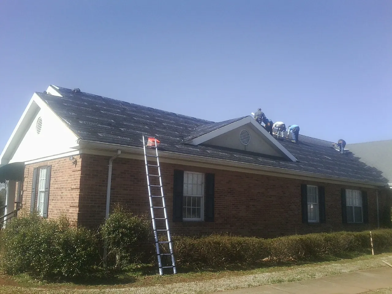 Crew tearing shingles off a brick ranch roof with a ladder set — Metal Roof Repair work by our crew in Smithville